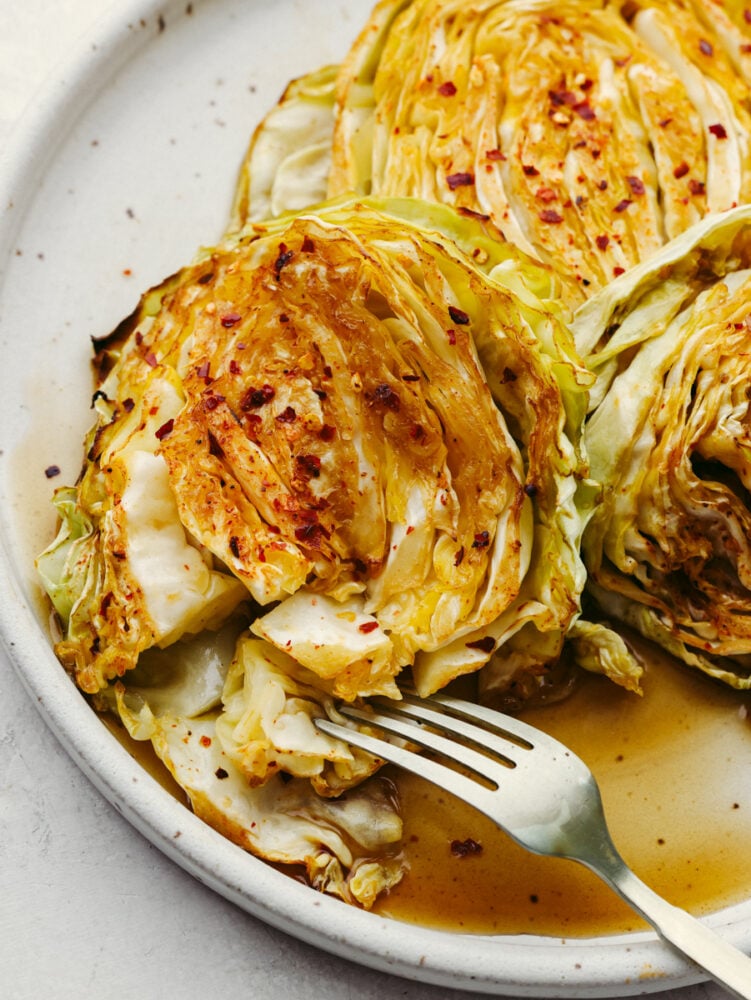 These tender cabbage steaks are so juicy and flavorful! Each bite is seasoned to perfection with soy sauce, chili powder, paprika, red pepper flakes, and a splash of lemon! Closeup of taking a bite of cabbage with a fork.