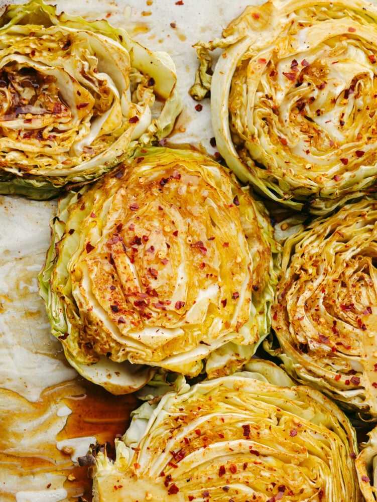 These tender cabbage steaks are so juicy and flavorful! Each bite is seasoned to perfection with soy sauce, chili powder, paprika, red pepper flakes, and a splash of lemon! Top-down view of cabbage steaks topped with soy sauce and seasonings.