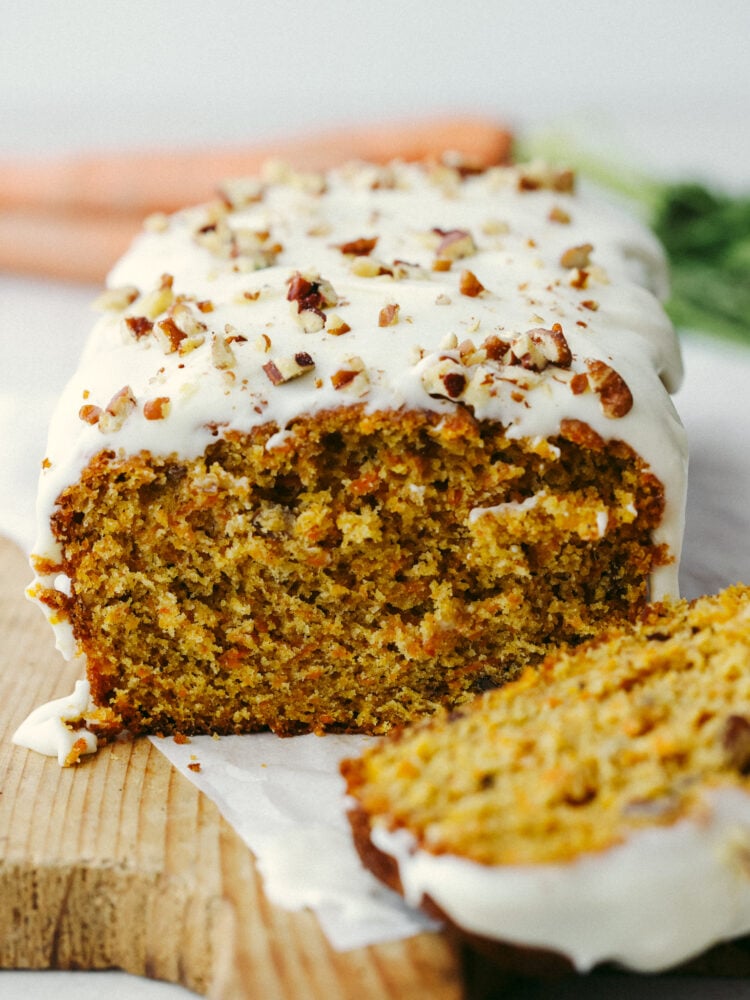 This carrot cake bread is to die for! It's moist and soft and has the most incredible flavor that tastes like cake, but it is half the work involved! This is perfect for Easter and springtime! A loaf of carrot cake bread with a slice taken out and a glaxe and pecans on top.