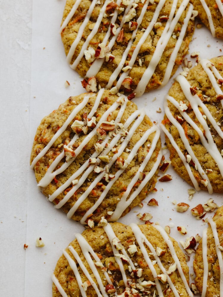 Carrot cake cookies are chewy and sweet with the best hint of warm spice! Drizzled with tangy cream cheese icing, you won't be able to get enough of this sweet treat! Top-down view of baked carrot cake cookies on parchment paper.