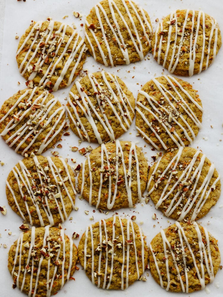 Carrot cake cookies are chewy and sweet with the best hint of warm spice! Drizzled with tangy cream cheese icing, you won't be able to get enough of this sweet treat! Top-down view of 12 cookies on parchment paper.