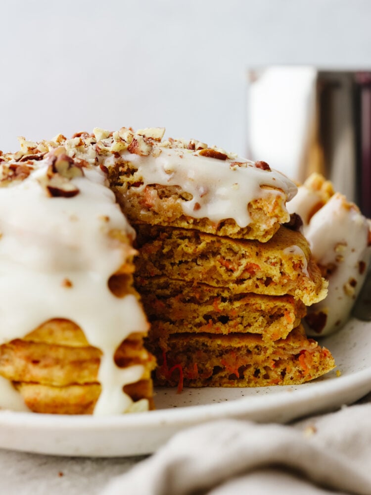 These carrot cake pancakes are fluffy, moist, and drizzled with a delicious cream cheese glaze that makes my mouth water! They will get gobbled up and fly off your table! A stack of carrot cake pancakes with a triangle bite cut out of them