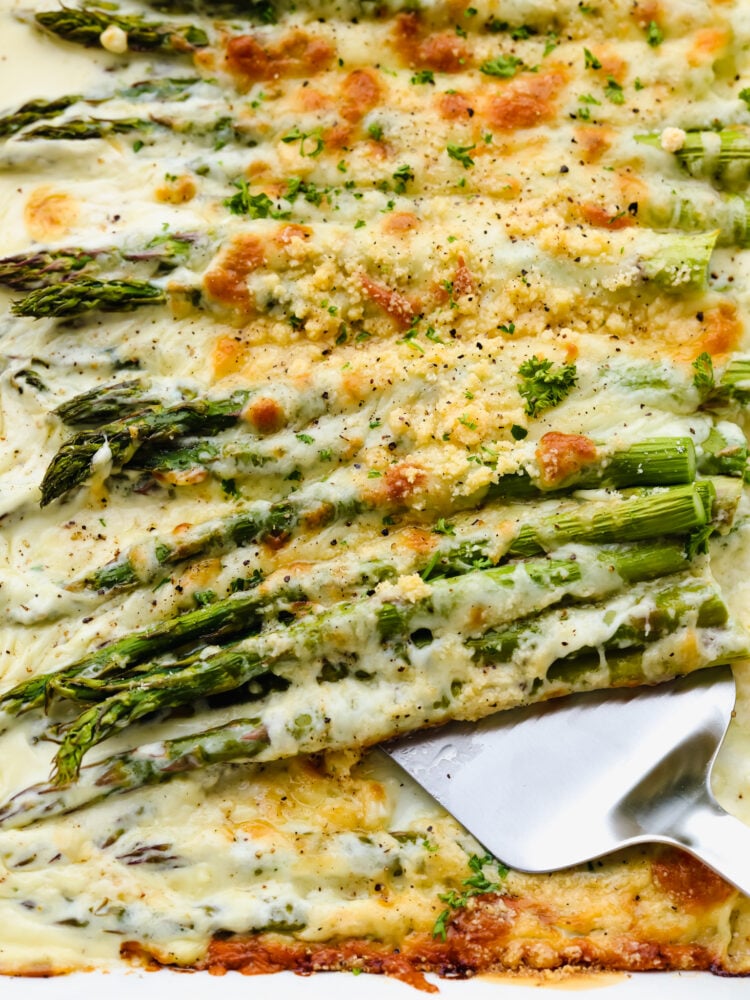 This cheesy baked asparagus will be the best side dish that you have ever had! Packed to the brim with flavor and melted cheese, this asparagus makes my mouth water just thinking of it! A close up of baked asparagus with cheese and a serving spoon.
