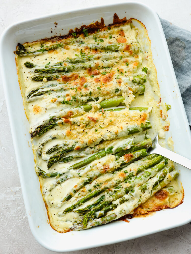 This cheesy baked asparagus will be the best side dish that you have ever had! Packed to the brim with flavor and melted cheese, this asparagus makes my mouth water just thinking of it! The top view of asparagus in a 9x13 baking dish, cooked ad ready to be served.