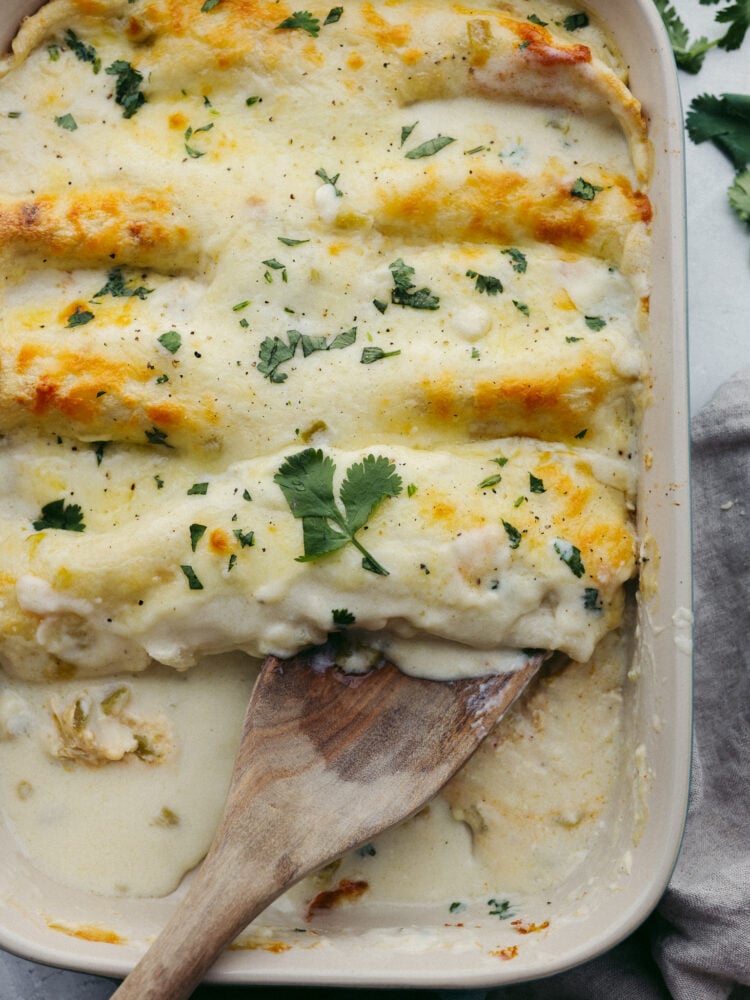 Creamy and filling, these white chicken enchiladas are perfect for any family dinner! They are ready in 30 minutes, so they are perfect for any of those busy, on-the-go nights! A baking pan filled with cooked white chicken enchiladas.
