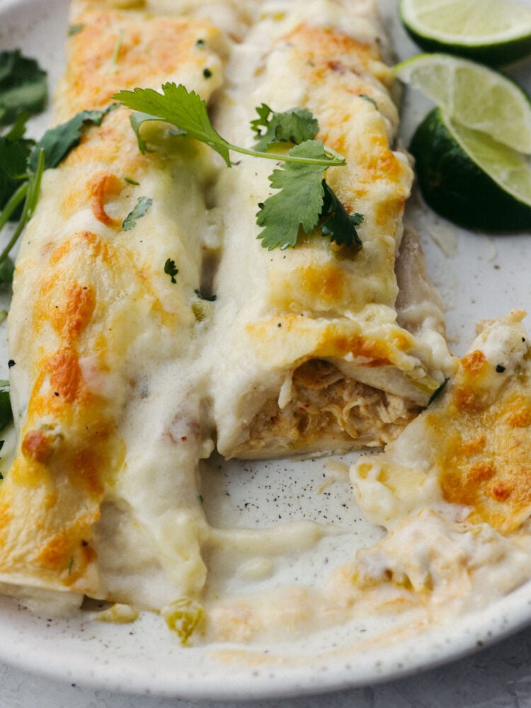 Creamy and filling, these white chicken enchiladas are perfect for any family dinner! They are ready in 30 minutes, so they are perfect for any of those busy, on-the-go nights! A white chicken enchilada on a plate, half eaten.