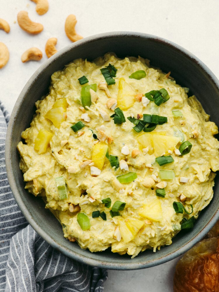 The flavor in this curry chicken salad is absolutely incredible! Infused with delicious spices and flavors, this twist on your classic chicken salad recipe is going to blow you away! The top view of curry chicken salad in a gray bowl, garnished with cashews and green onions.