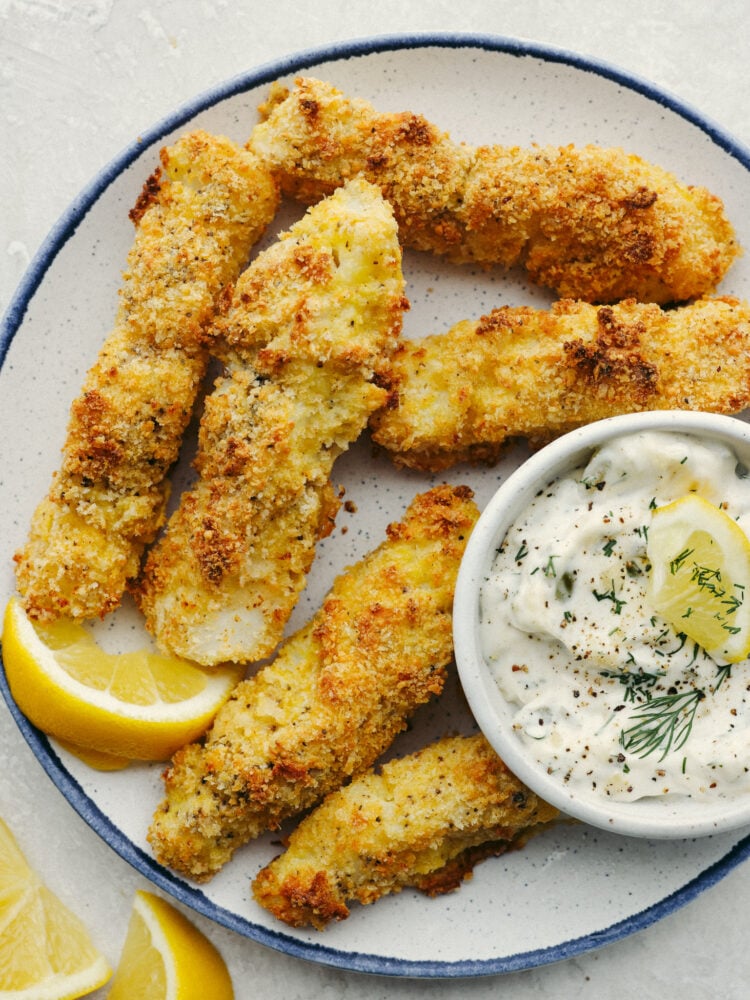 Oven-baked fish sticks are crispy, tender, and SO good! Coated with breadcrumbs and delicious seasoning, these fish sticks are packed with flavor and a recipe that the whole family will enjoy! A plate of baked fish sticks and tartar saice.