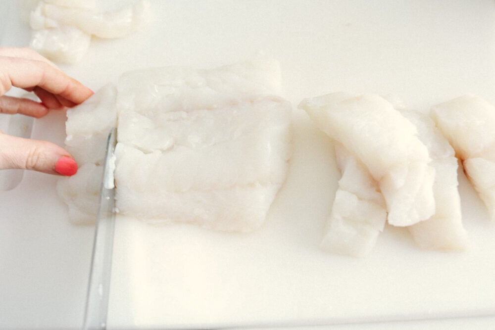Oven-baked fish sticks are crispy, tender, and SO good! Coated with breadcrumbs and delicious seasoning, these fish sticks are packed with flavor and a recipe that the whole family will enjoy! A picture of cod on a cutting board being cut into slices.