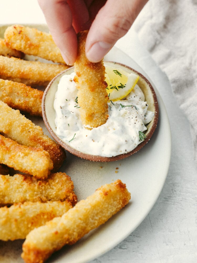You're going to love how easy it is to make frozen fish sticks in the air fryer! They're golden, delicious, and ready for your favorite dips. Dipping a fish stick in tartar sauce.