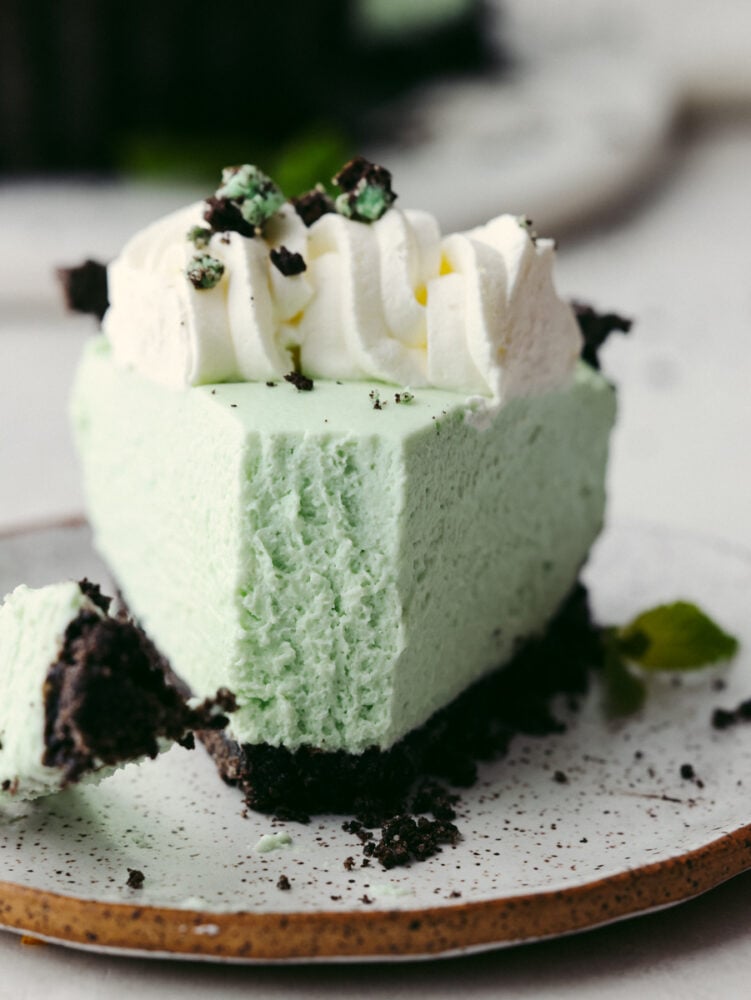 This chilled, minty pie grasshopper pie has a creamy filling sitting on an Oreo cookie crust. The taste and smooth texture are perfect and will have just about anyone coming back for seconds! A slice of grasshopper pie on a plate with a bite cute out of the tip of the slice.