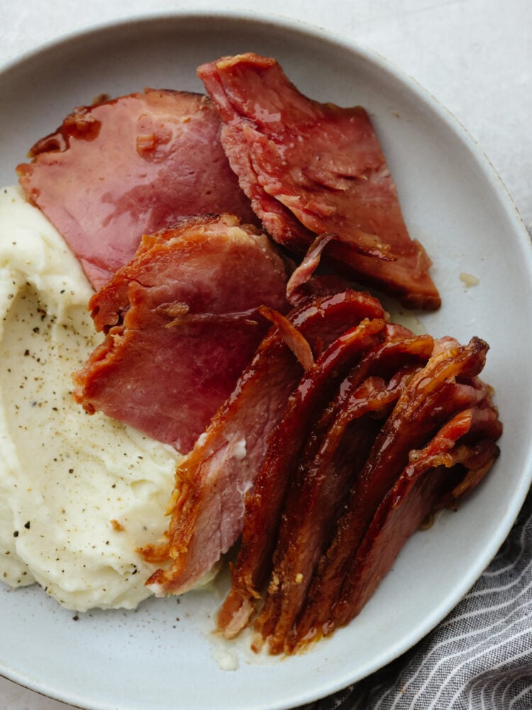 This instant pot ham is juicy, full of flavor, and cooked so that there is a caramelized glaze, making this ham taste like a slice of heaven! It will have every guest at your dinner table asking for the recipe! Instant pot ham on a plate with some mashed potatoes.