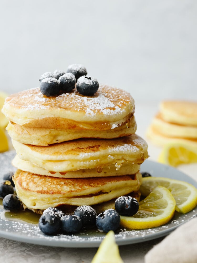 These lemon ricotta pancakes are the best pancakes that you will EVER eat! They are soft, delicious, and have the slightest hint of lemon flavor that will go perfect with just about any topping that you put on them! A stack of lemon ricotta pancakes on a gray plate that are topped with blueberries and powdered sugar.