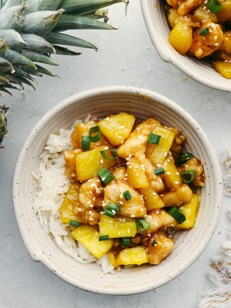 This crispy, saucy chicken is every pineapple lover's dream! Pineapple chicken is the best mix of sweet and savory. It's a quick and easy dinner that your family will go crazy over! Pineapple chicken served over rice in a white bowl.