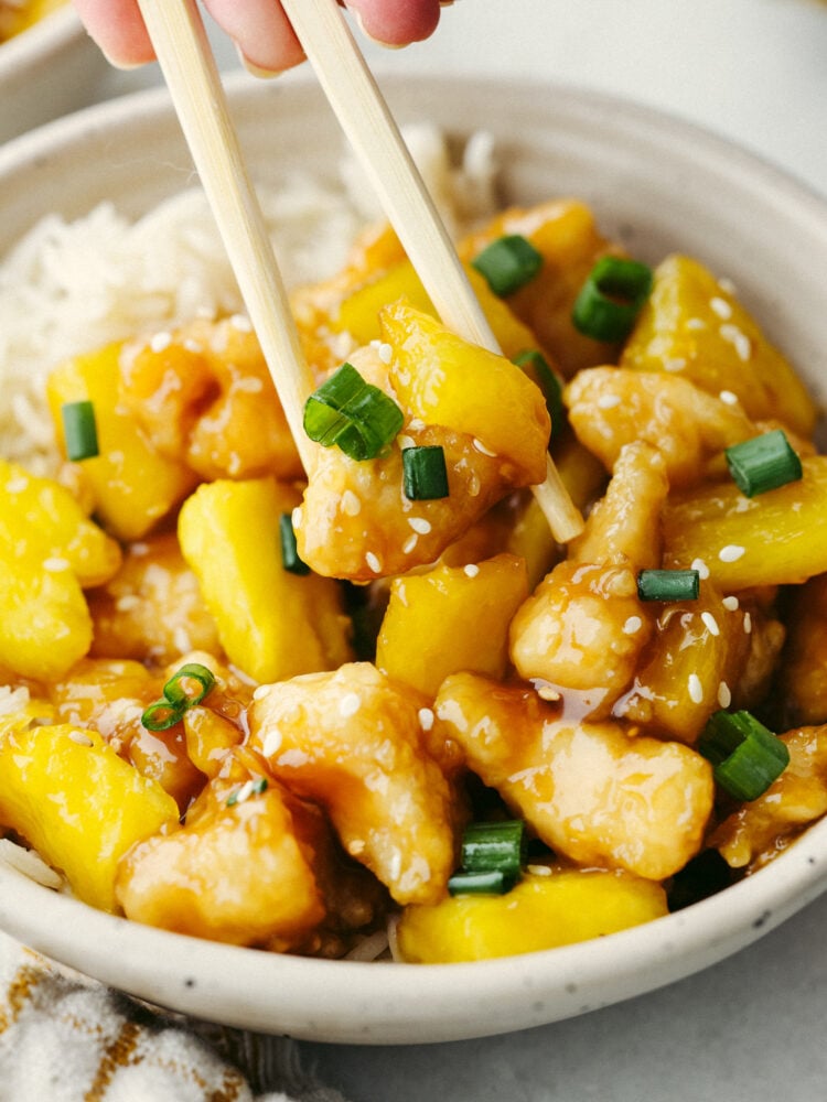 This crispy, saucy chicken is every pineapple lover's dream! Pineapple chicken is the best mix of sweet and savory. It's a quick and easy dinner that your family will go crazy over! Picking up a piece of pineapple chicken with chopsticks.