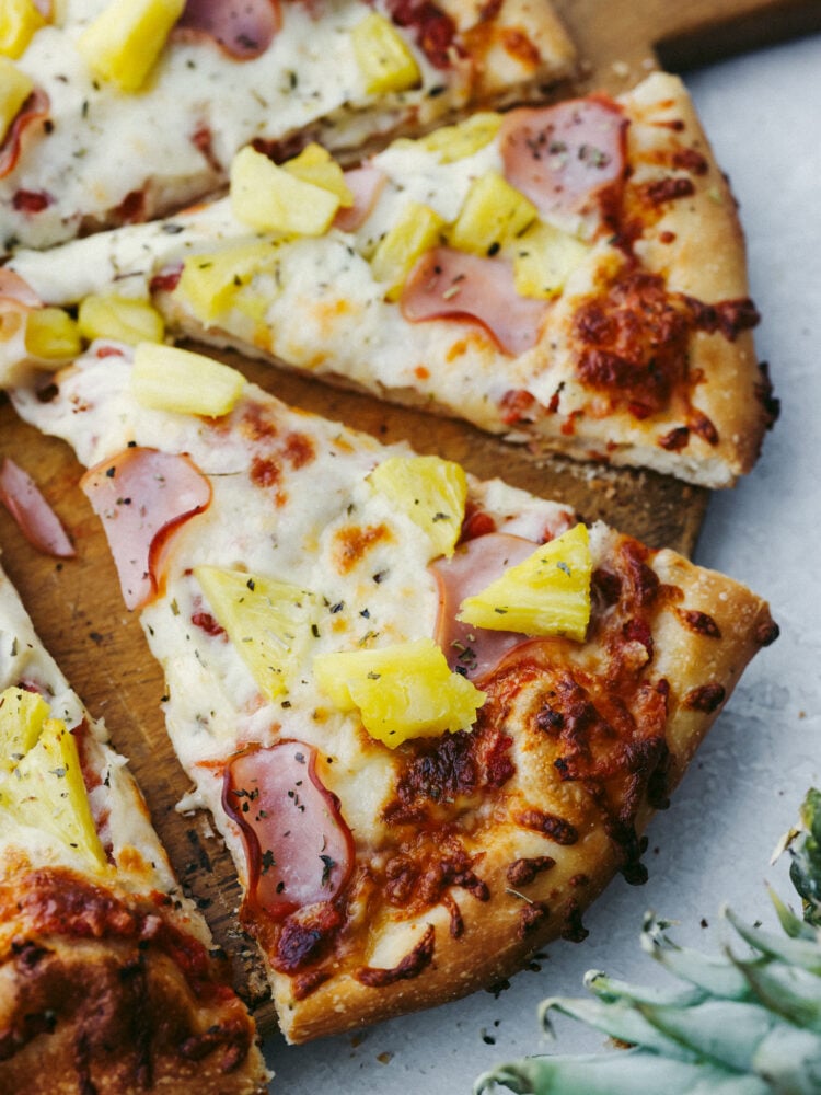 The perfect combination of sweet and savory, Hawaiian pizza is a must-try for your next pizza night! Topped with melty mozzarella, Canadian bacon, pineapple, and Italian herbs, each slice is bursting with flavor! Closeup of 2 slices of pizza.