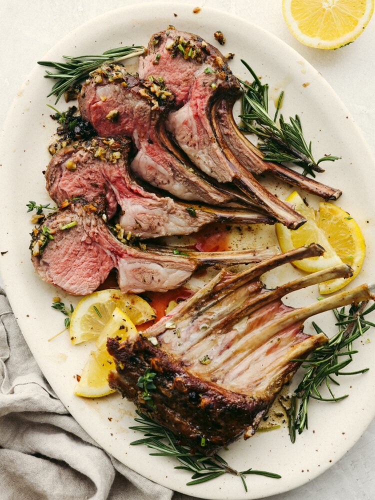 Mouthwatering and delicious, this garlic herb-crusted rack of lamb is the most amazing main dish that you could ever offer to your guests! Beautiful, delicious, and impressive; it checks all of the boxes! A rack of lamb cut and plated with some lemons and herbs.
