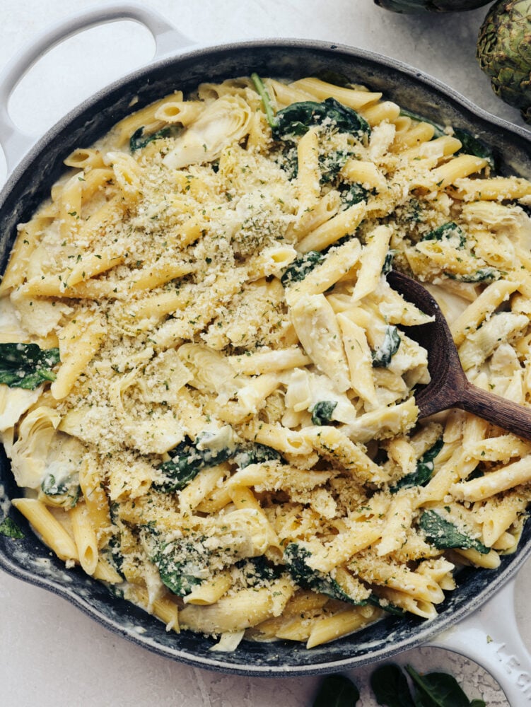 Spinach artichoke pasta is the perfect marriage of hearty and fresh! These ingredients complement each other and blend together so seamlessly that you will be asking for seconds in no time! A skillet filled with spinach artichoke pasta and topped with some bread crumbs.