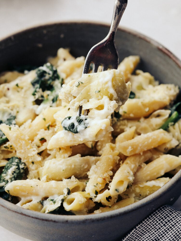Spinach artichoke pasta is the perfect marriage of hearty and fresh! These ingredients complement each other and blend together so seamlessly that you will be asking for seconds in no time! A close up of a bowl filled with spinach artichoke pasta with a fork in it.