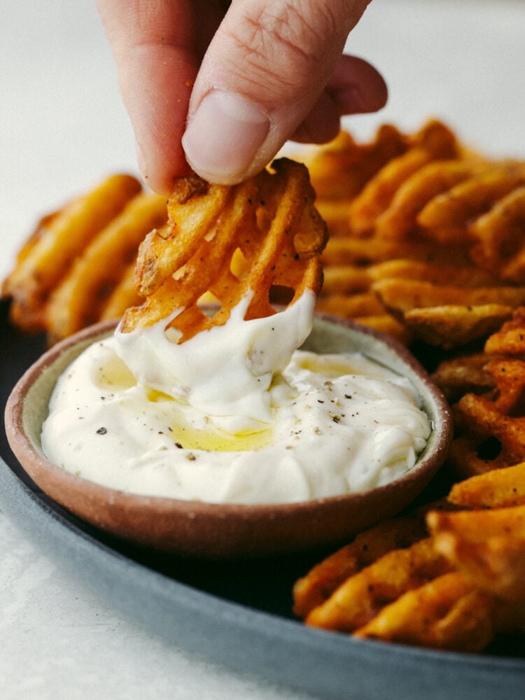 This garlic aioli sauce is dreamy! The hint of lemon flavor combined with garlic has my mouth watering. It's packed with enough flavor to make anything that you dip into it that much more delicious. A waffle fry being dipped into garlic aioli sauce.