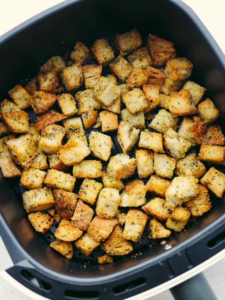 These quick and easy air fryer croutons will give your salads and recipes that "wow" factor! A fresh loaf of bread cubed, seasoned, and air fried to perfection. Hero image of croutons in the basket of an air fryer.
