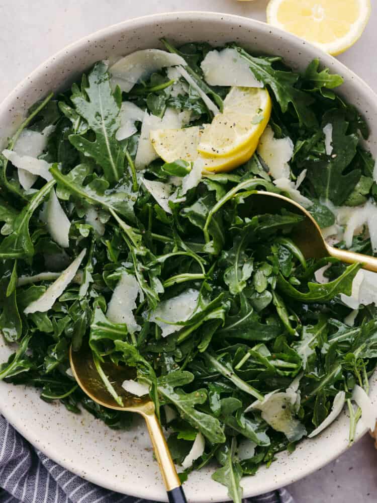 This classic and simple arugula salad will elevate any meal! With only a few ingredients, it comes together quickly, and the flavors of the arugula, Parmesan Reggiano, and lemon vinaigrette really shine together. Top-down view of arugula salad, garnished with lemon and ready to serve.