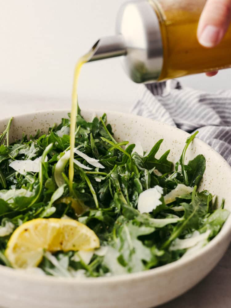 This classic and simple arugula salad will elevate any meal! With only a few ingredients, it comes together quickly, and the flavors of the arugula, Parmesan Reggiano, and lemon vinaigrette really shine together. Closeup of lemon vinaigrette being drizzled over salad.