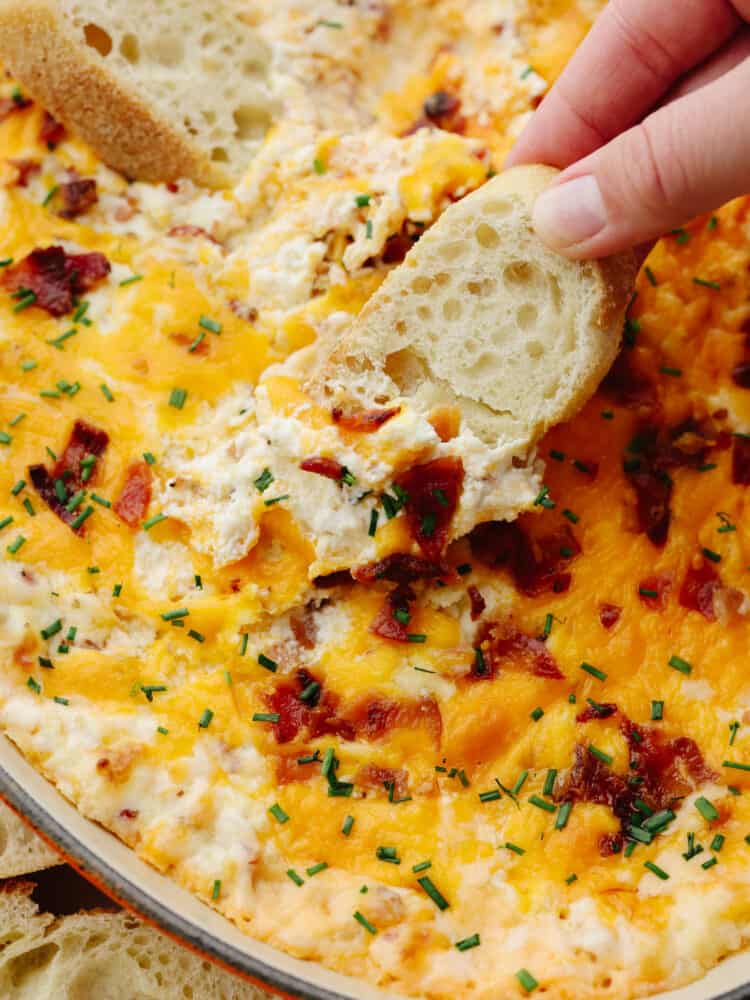 Creamy and packed with flavor, this baked bacon dip is to die for! You will love all of the ingredients that come together to make it the best dip that you've ever had! A close up of a slice of french bread being dipped into baked bacon dip.