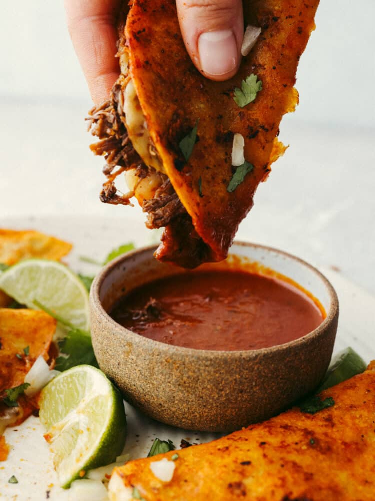 These Birria tacos are packed full of flavor! They are filled with beef and Mexican flavorings that are so delicious that you will definitely need to come to this meal hungry because you will for sure be asking for seconds! A birria taco being dipped into sauce.