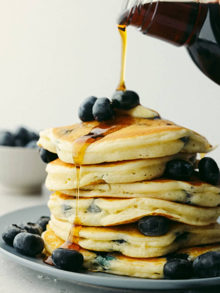 Blueberry pancakes are a classic breakfast option for a good reason... They are the best! Soft, fluffy, and packed with fresh, juicy blueberries, you won't be able to stop at just one! Syrup being poured onto a stack of blueberry pancakes.