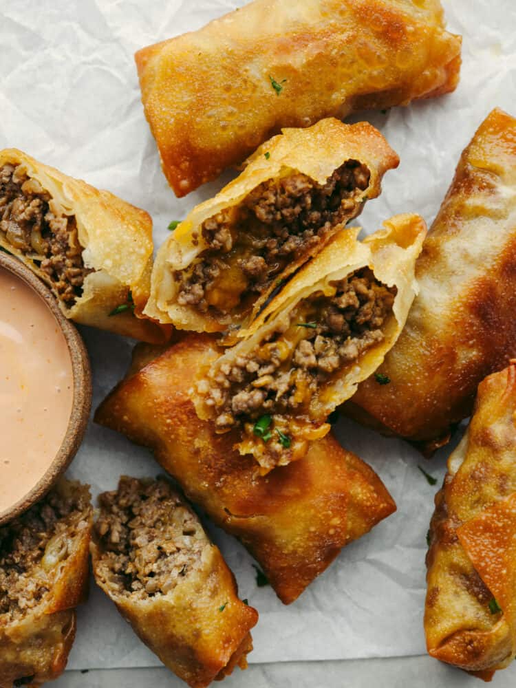 Cheeseburger eggrolls have all the beefy, cheesy goodness of a burger but inside a crispy shell! Make this delicious appetizer for your next get-together and I assure you, it will be a huge hit! Top-down view of eggrolls cut into halves so the filling can be seen.