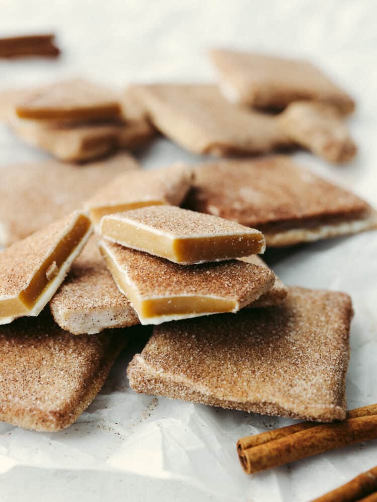 This churro toffee is covered in delicious white chocolate, sprinkled with cinnamon sugar, and leaves your mouth watering after just one bite! It's better than the stuff found at Disneyland, AND you can make it at home! A zoomed in shot of toffee that is broken into pieces on parchment paper.