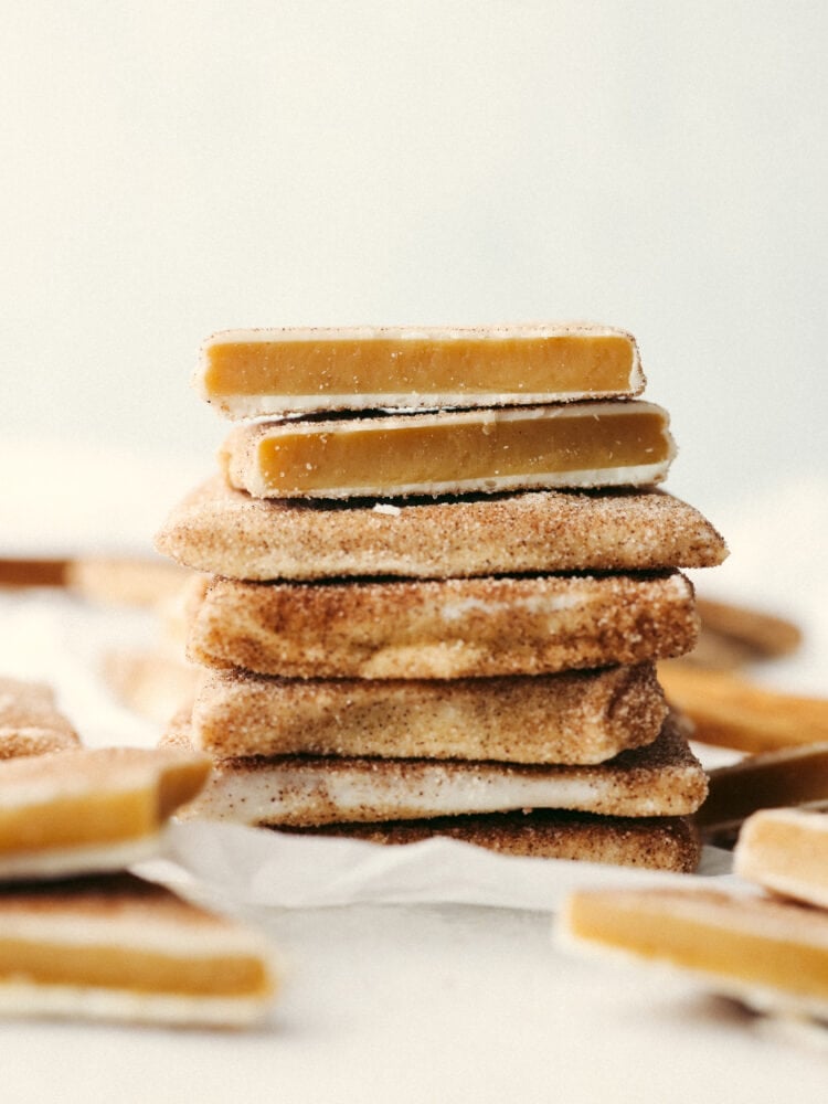This churro toffee is covered in delicious white chocolate, sprinkled with cinnamon sugar, and leaves your mouth watering after just one bite! It's better than the stuff found at Disneyland, AND you can make it at home! A stack of churro toffee. The top piece is broken in half so that you can see the inside.
