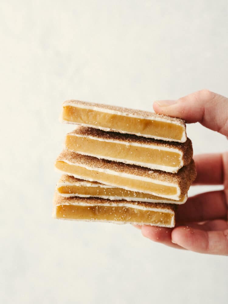 This churro toffee is covered in delicious white chocolate, sprinkled with cinnamon sugar, and leaves your mouth watering after just one bite! It's better than the stuff found at Disneyland, AND you can make it at home! Someone holding a stack of churro toffee.