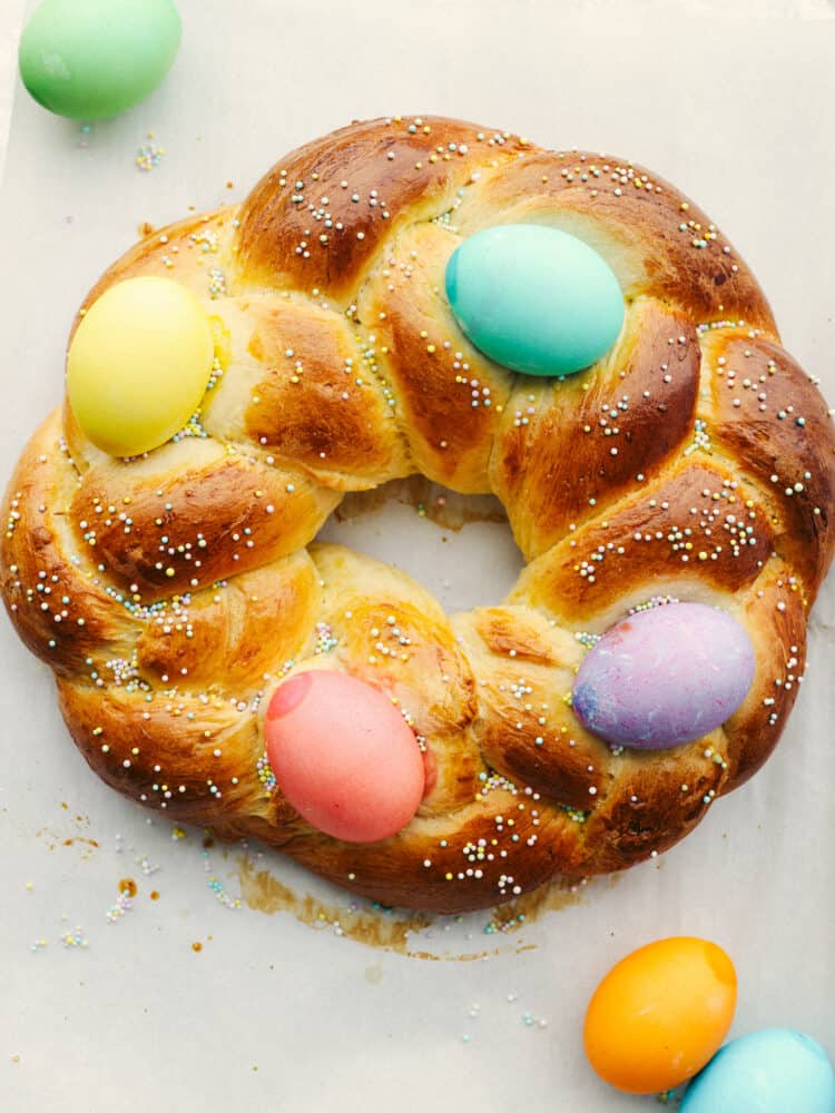 Easter bread is fluffy, sweet, and almost too cute to eat! This festive bread is sure to be a hit with its soft, tender texture and colorful presentation! Top-down view of an Easter bread wreath, decorated with sprinkles and Easter eggs.
