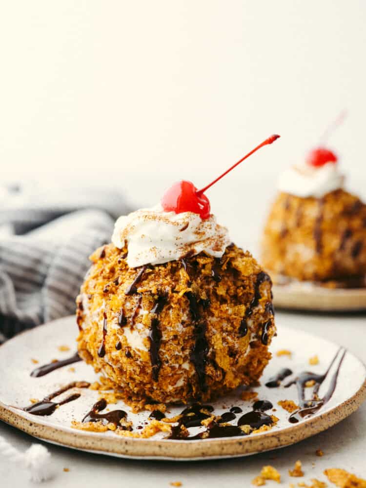 Get your sweet tooth ready, this fried ice cream recipe is the perfect combination of crispy and creamy! Vanilla ice cream is coated with buttery cinnamon sugar cornflakes for a texture your tastebuds will go crazy over! A globe-shaped fried ice cream topped with whipped cream, a maraschino cherry, and chocolate drizzle.
