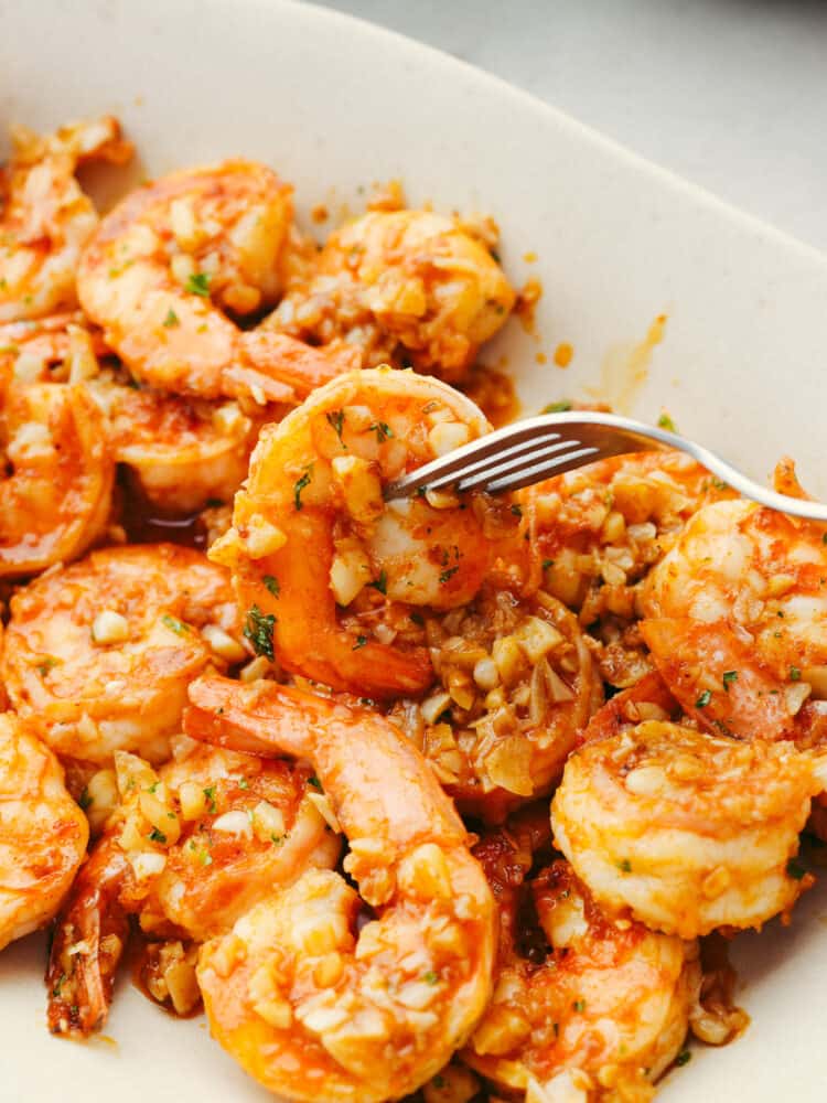 Hawaiian-style garlic shrimp is cooked up in a dreamy garlic butter sauce. Inspired by the food trucks in Hawaii, the punch of savory flavor in each bite will have you feeling like you're on vacation! A piece of shrimp being skewered with a fork.