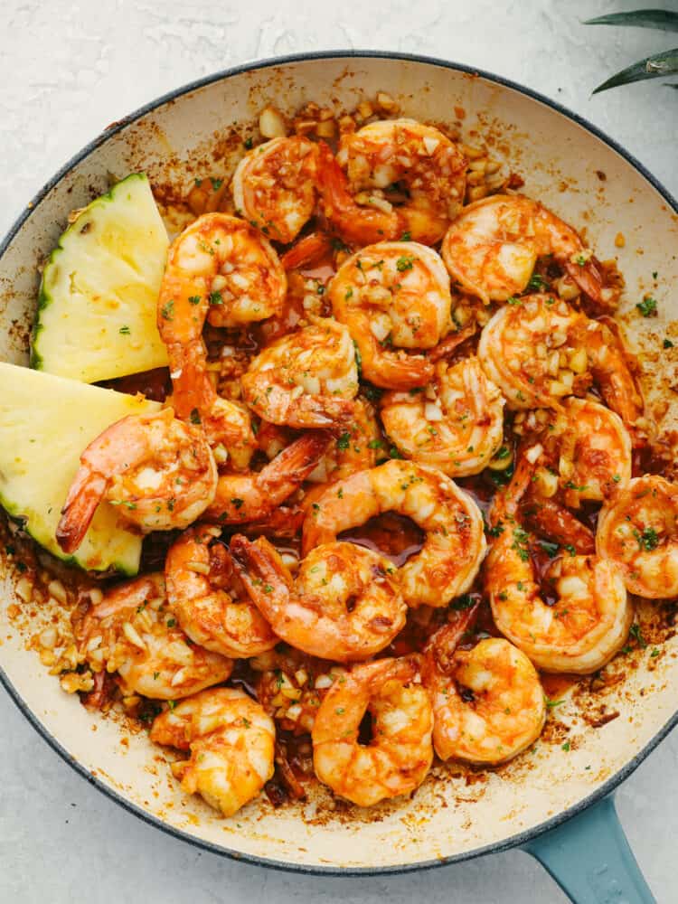 Hawaiian-style garlic shrimp is cooked up in a dreamy garlic butter sauce. Inspired by the food trucks in Hawaii, the punch of savory flavor in each bite will have you feeling like you're on vacation! Top-down view of garlic shrimp in a white and blue skillet.
