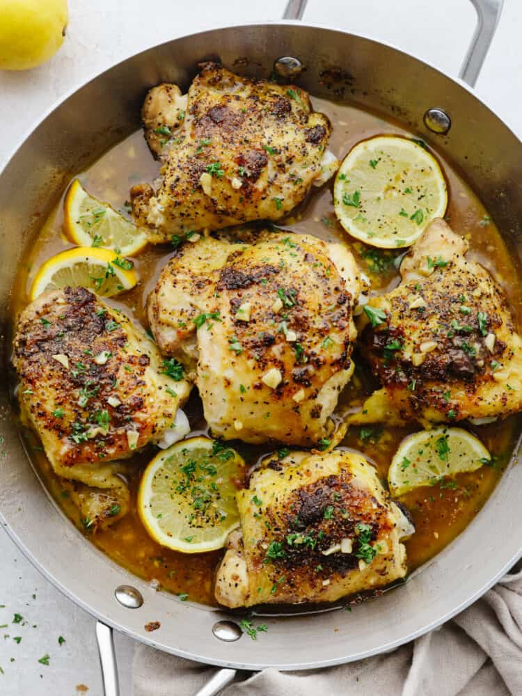 Juicy chicken is coated in lemon pepper seasoning and baked to tender perfection in this easy recipe. The brown butter garlic lemon sauce on top is absolutely incredible! Top-down view of lemon pepper chicken, garnished with lemon, in a metal skillet.