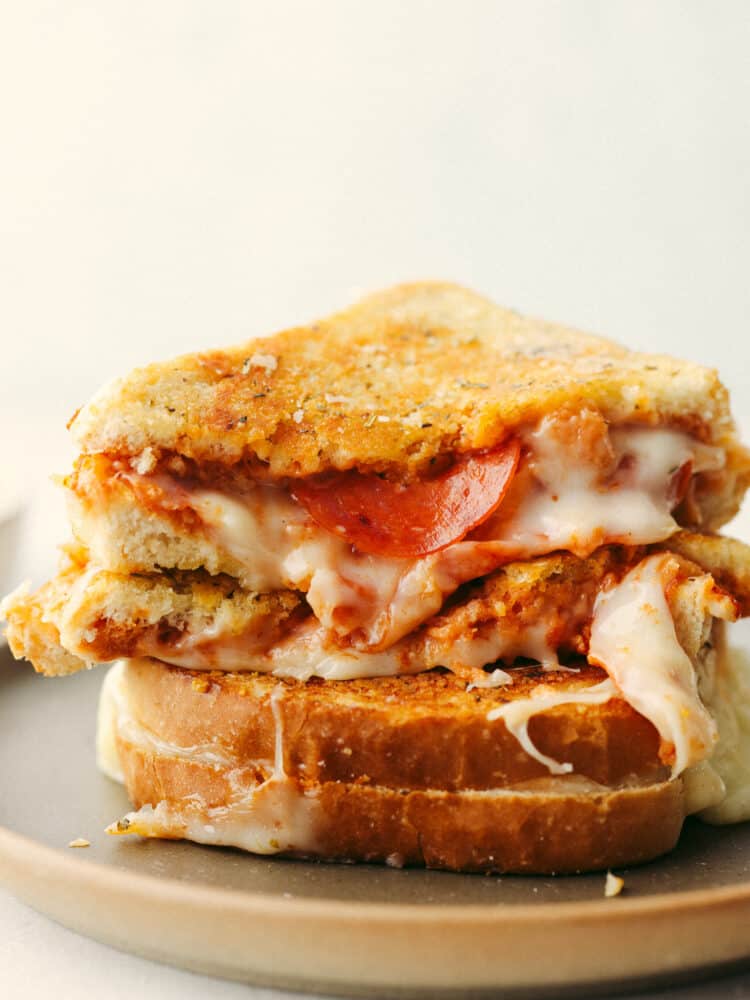 This amazing pizza grilled cheese has all the melty goodness of a classic grilled cheese sandwich combined with the flavor of pepperoni pizza! It's a quick and easy meal everyone in your family will love. 2 triangle-cut halves of a pizza grilled cheese stacked on top of each other.