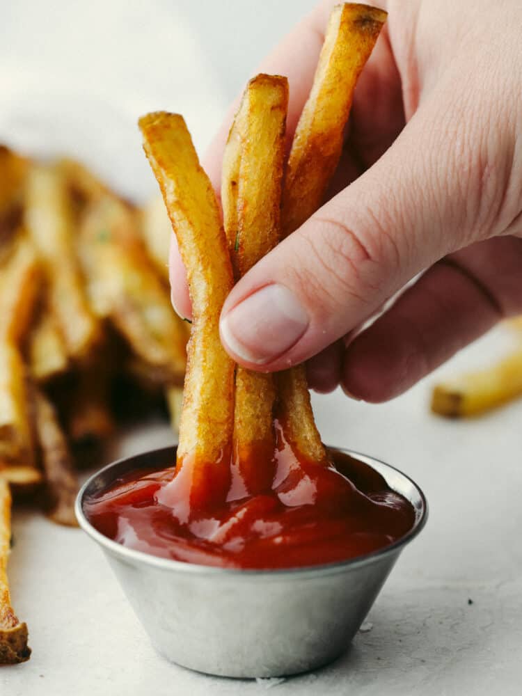 Try out these amazing Pommes Frites that are seasoned and cooked to perfection! They are the perfect side dish for just about anything. After all, everyone loves fries! Fries being dipped into ketchup.