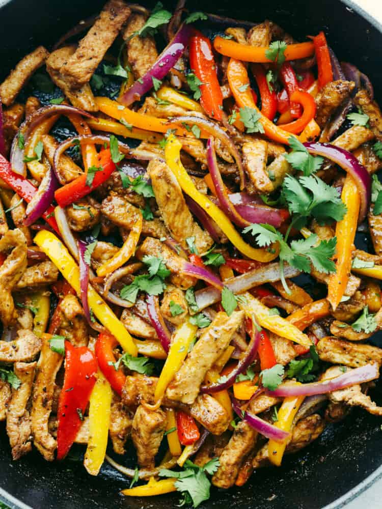 These pork fajitas are bursting with all your favorite Mexican flavors! The lean pork, fresh peppers and onions, fajita seasonings, and soft tortillas will have you coming back for more! Close up photo of sliced and cooked pork, peppers, and onions. Garnished with chopped cilantro.