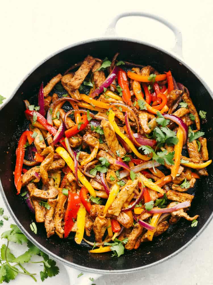These pork fajitas are bursting with all your favorite Mexican flavors! The lean pork, fresh peppers and onions, fajita seasonings, and soft tortillas will have you coming back for more! Cooked and seasoned pork, peppers and onions in a cast iron skillet, garnished with cilantro.