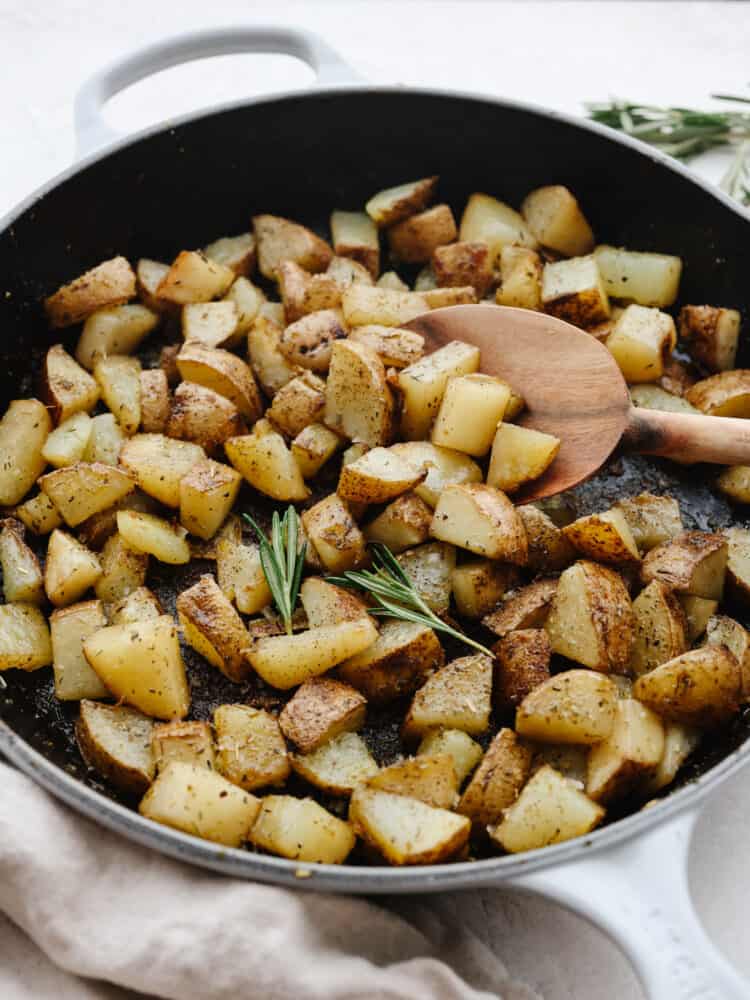 Tossed with Italian herbs and olive oil, this simple pan-fried potato dish is going to be a new dinner favorite. Serve them for breakfast or alongside a hearty dinner! Chopped, cooked potatoes being stirred with a wooden spoon in a shallow skillet.