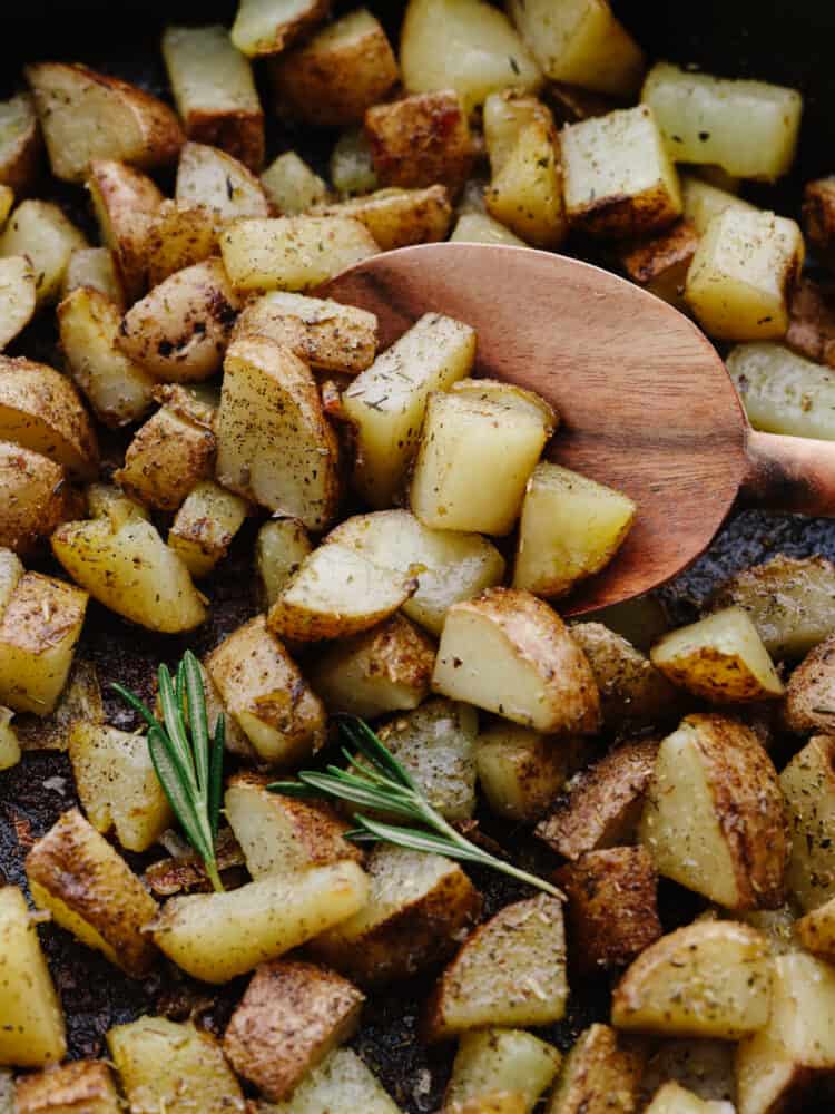 Tossed with Italian herbs and olive oil, this simple pan-fried potato dish is going to be a new dinner favorite. Serve them for breakfast or alongside a hearty dinner! Potato chunks being scooped up with a wooden spoon.