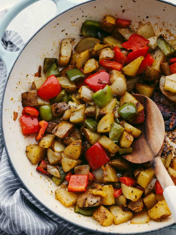 These breakfast potatoes make the best hearty and delicious breakfast! Filled with peppers, onions, and potatoes that are all coated with delicious homemade seasoning, this savory dish will become a family favorite! A skillet with cooked potaotes, peppers and onions with a wooden spoon scooping some up.