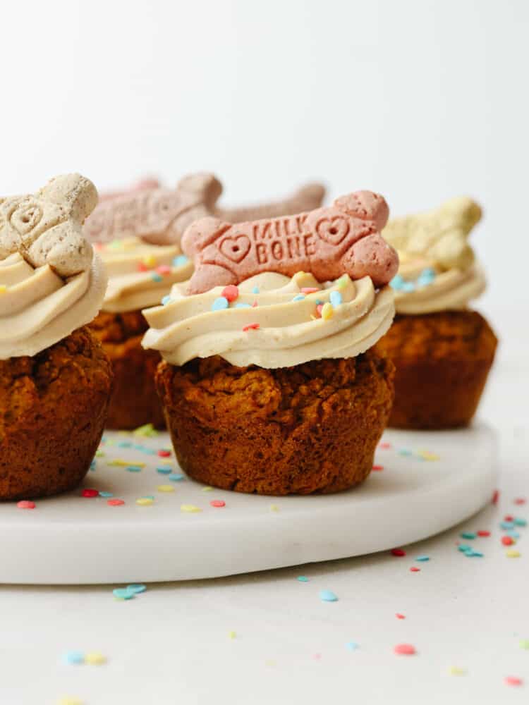 Pupcakes are a dog-friendly dessert your 4-legged friend will go crazy over! They're super easy to make and full of healthy ingredients for your pup! Multiple frosted pupcakes on a cake board.