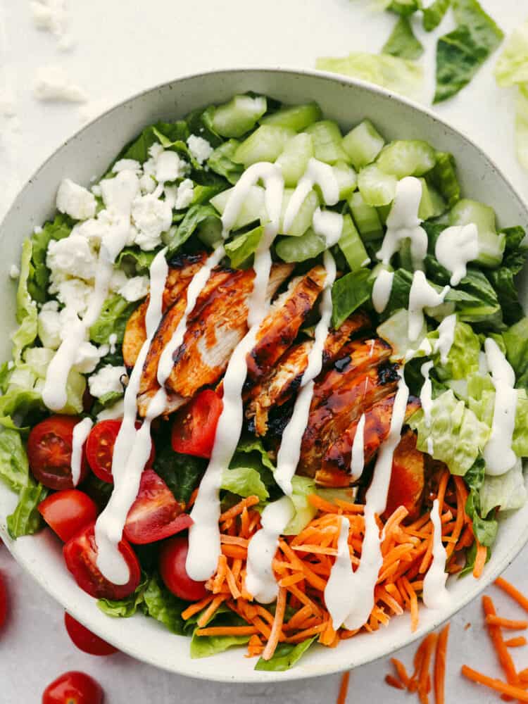This buffalo chicken salad is packed with fresh vegetables, feta cheese, and the perfect buffalo chicken. Layer this with some homemade dressing, and you'll have your new go-to salad recipe! The top view of buffalo chicken salad in a bowl. Ranch dressing is drizzled on top.