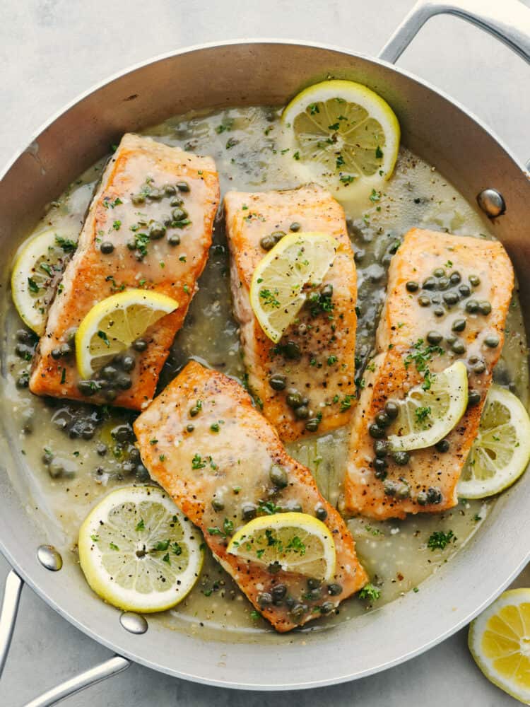 This easy salmon piccata is a delicious yet elegant meal that is great for a weeknight meal or for when you have guests over. The flakey pan-seared salmon nestled in a bed of a creamy lemon and caper sauce will definitely be a crowd-pleaser! A pan filled witl samon filets covered in lemons and capers.