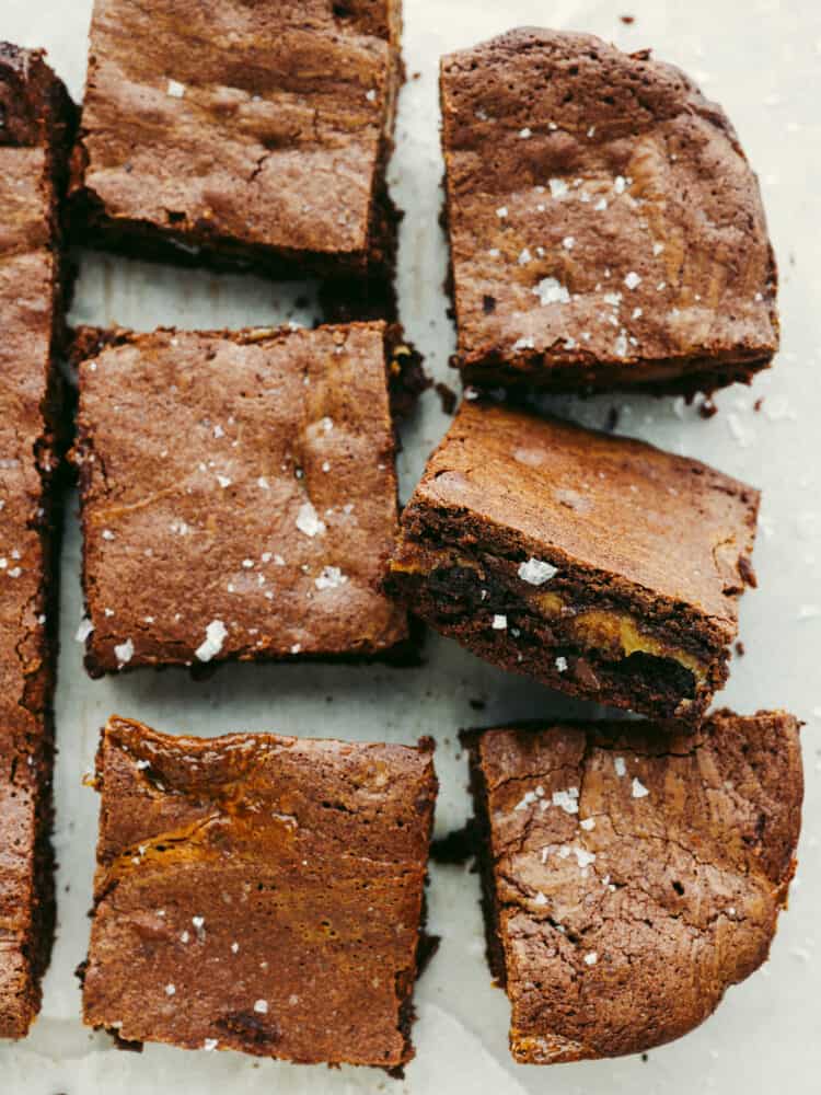 These salted caramel brownies are perfectly fudgy and moist brownies with an oozing salted caramel center. These will be one of the best brownies you sink your teeth into! The top view of cooked brownies and sliced brownies on some parchment paper.